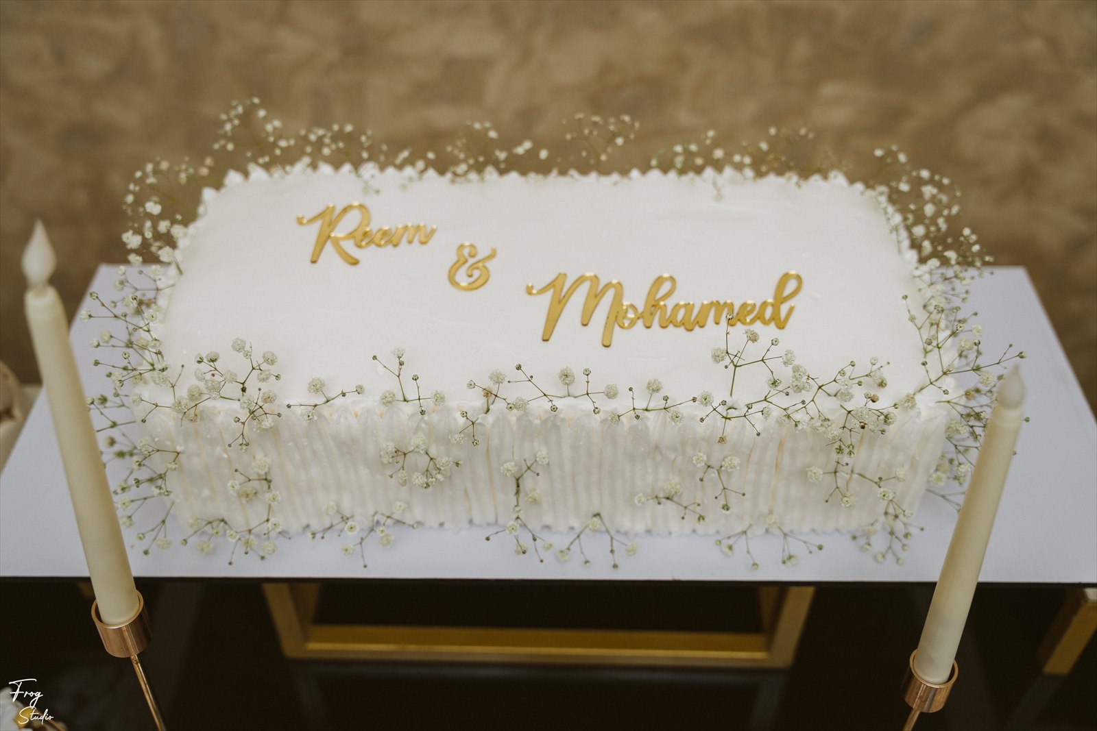 Close view of the long white engagement cake piped with the gold names Reem and Mohamed