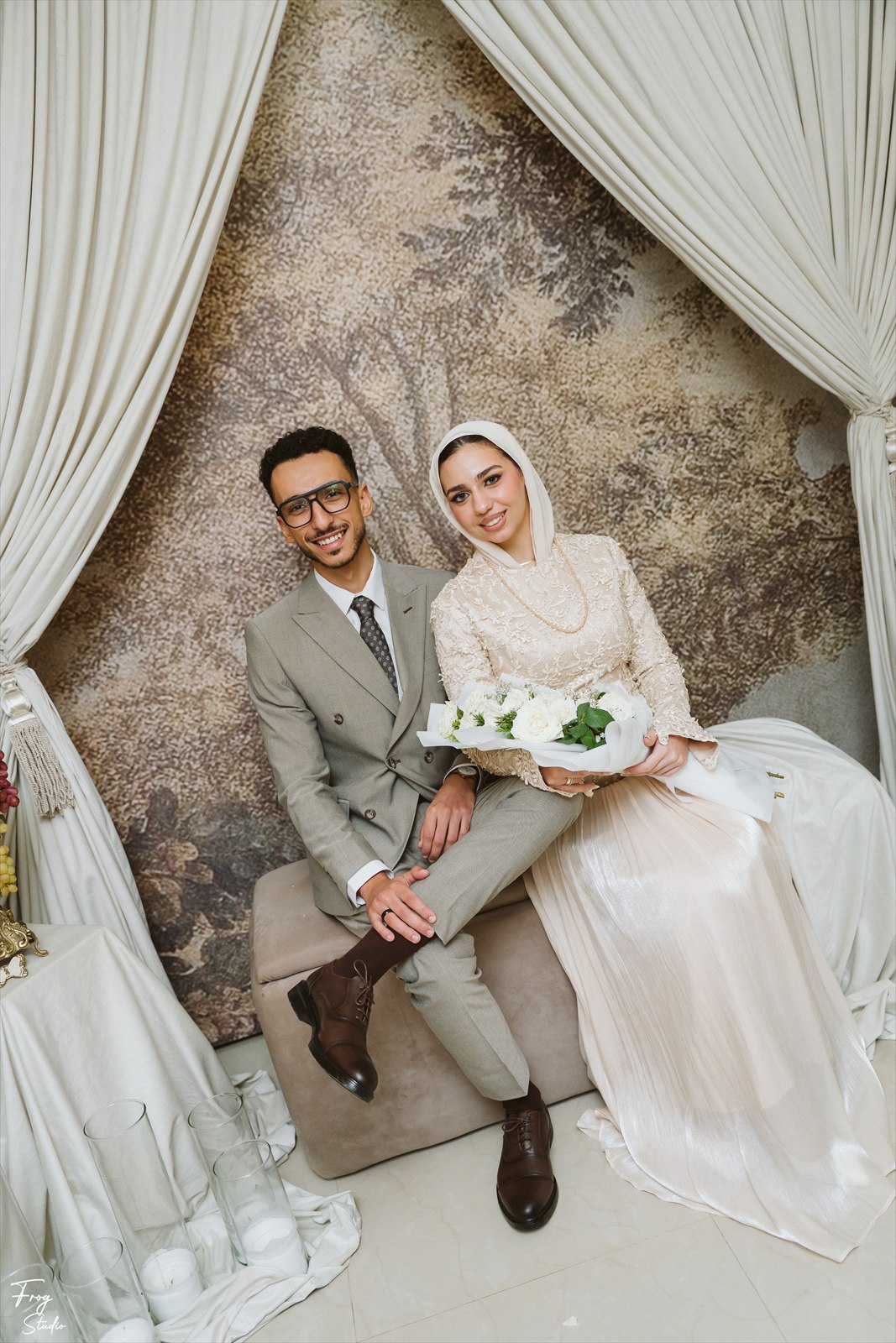 Reem and Mohamed standing side by side holding hands in front of the draped backdrop
