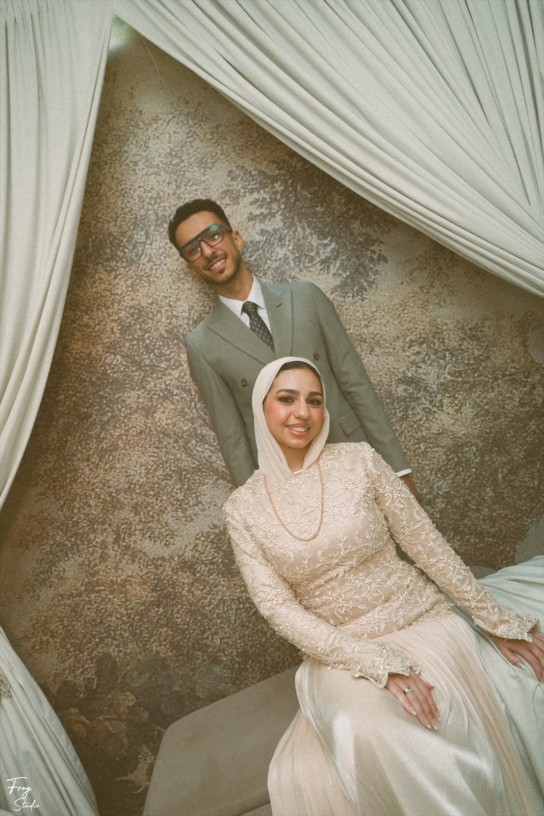 Reem seated in a beaded ivory lace gown and pearl headpiece, wearing a delicate gold chain
