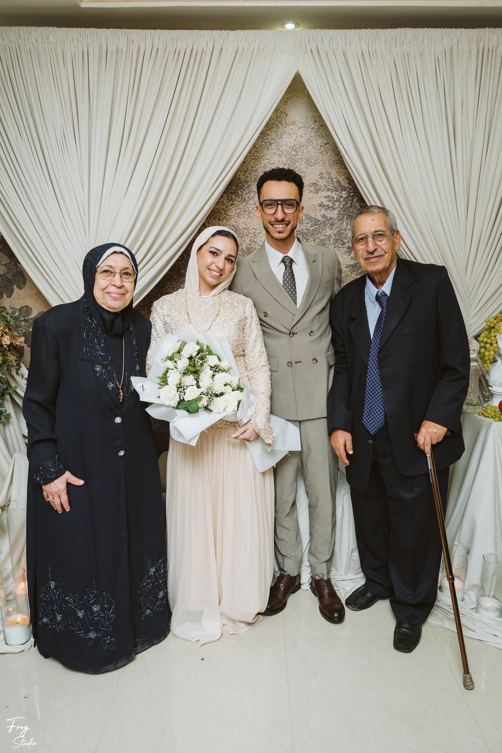Mohamed and Reem standing with Mohamed&rsquo;s grandmother in a navy embroidered coat and his grandfather in a dark suit