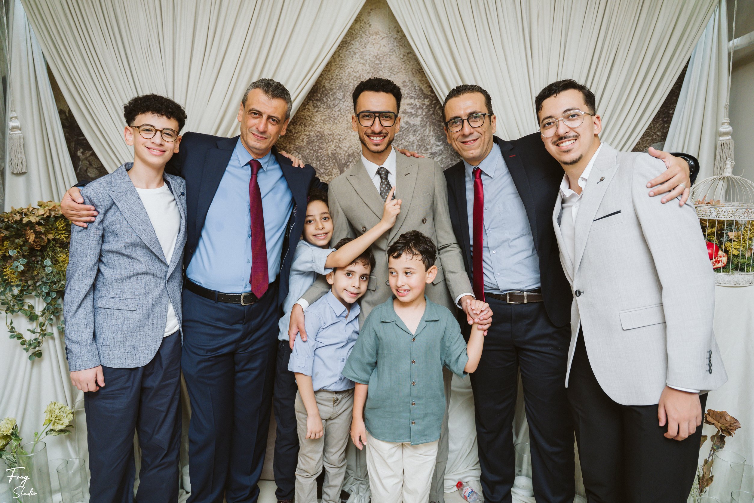 A group of men and boys in suits and shirts posing together in front of the draped backdrop