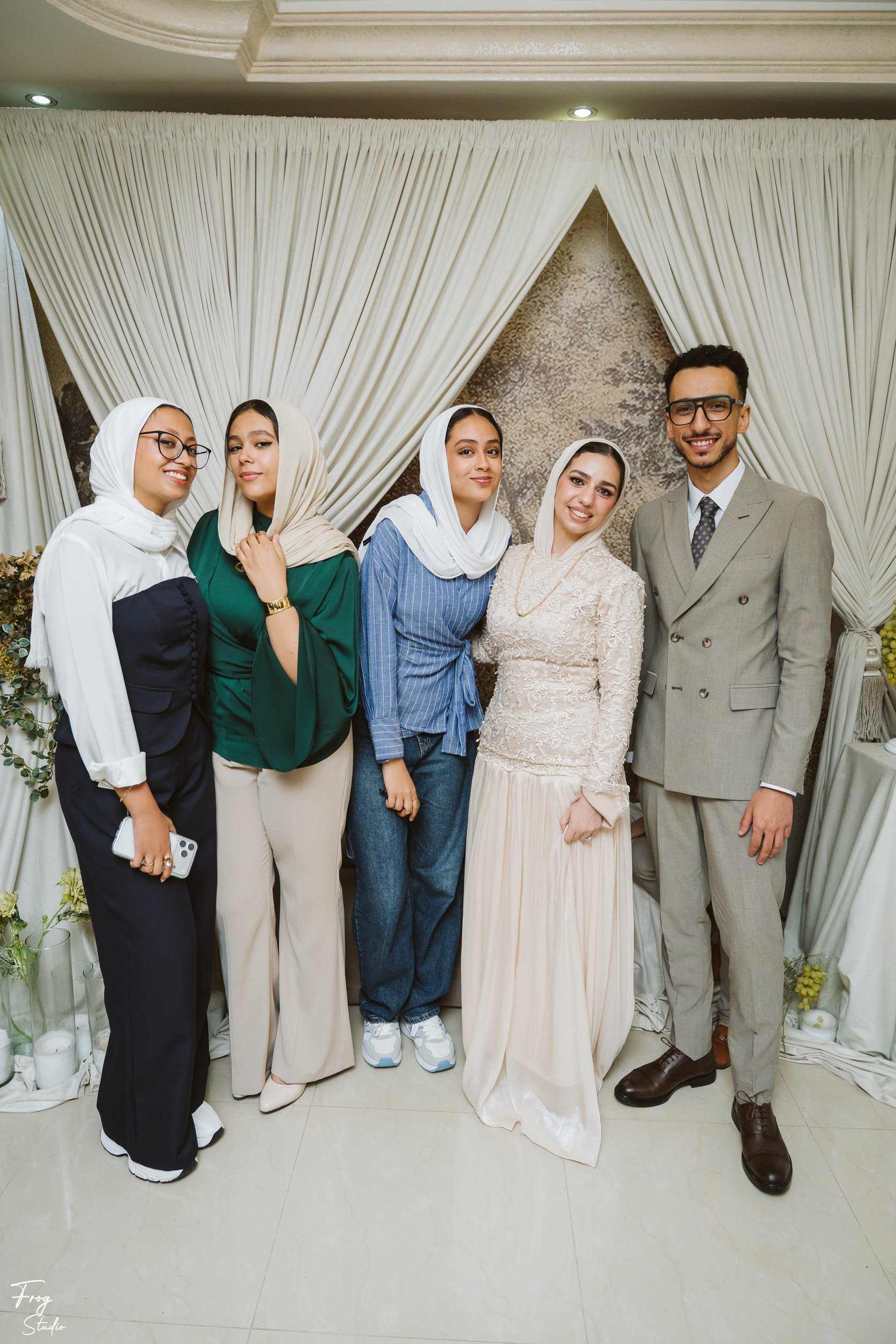 Four ladies in elegant dresses and hijabs standing with Mohamed at the engagement backdrop
