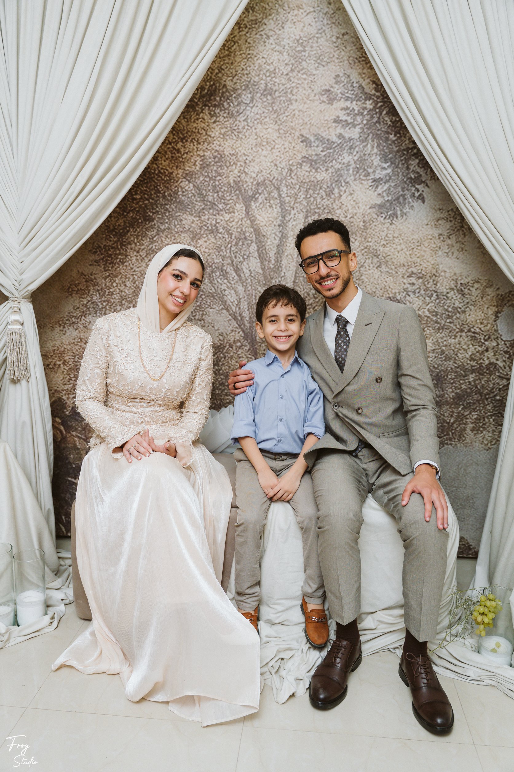 Mohamed and Reem seated on the sofa with a young boy between them, all smiling