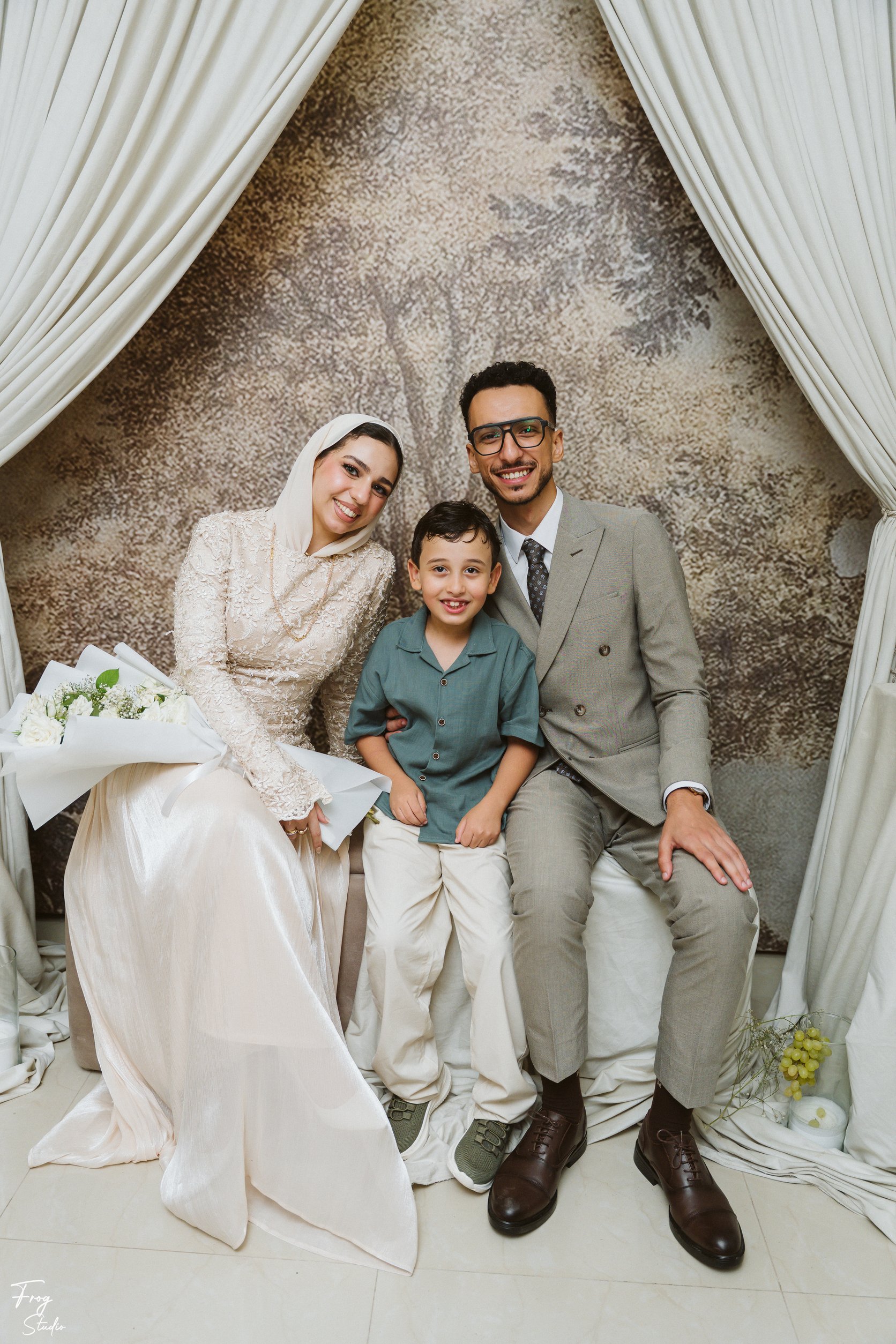 Mohamed and Reem seated either side of a smiling boy with the white rose bouquet