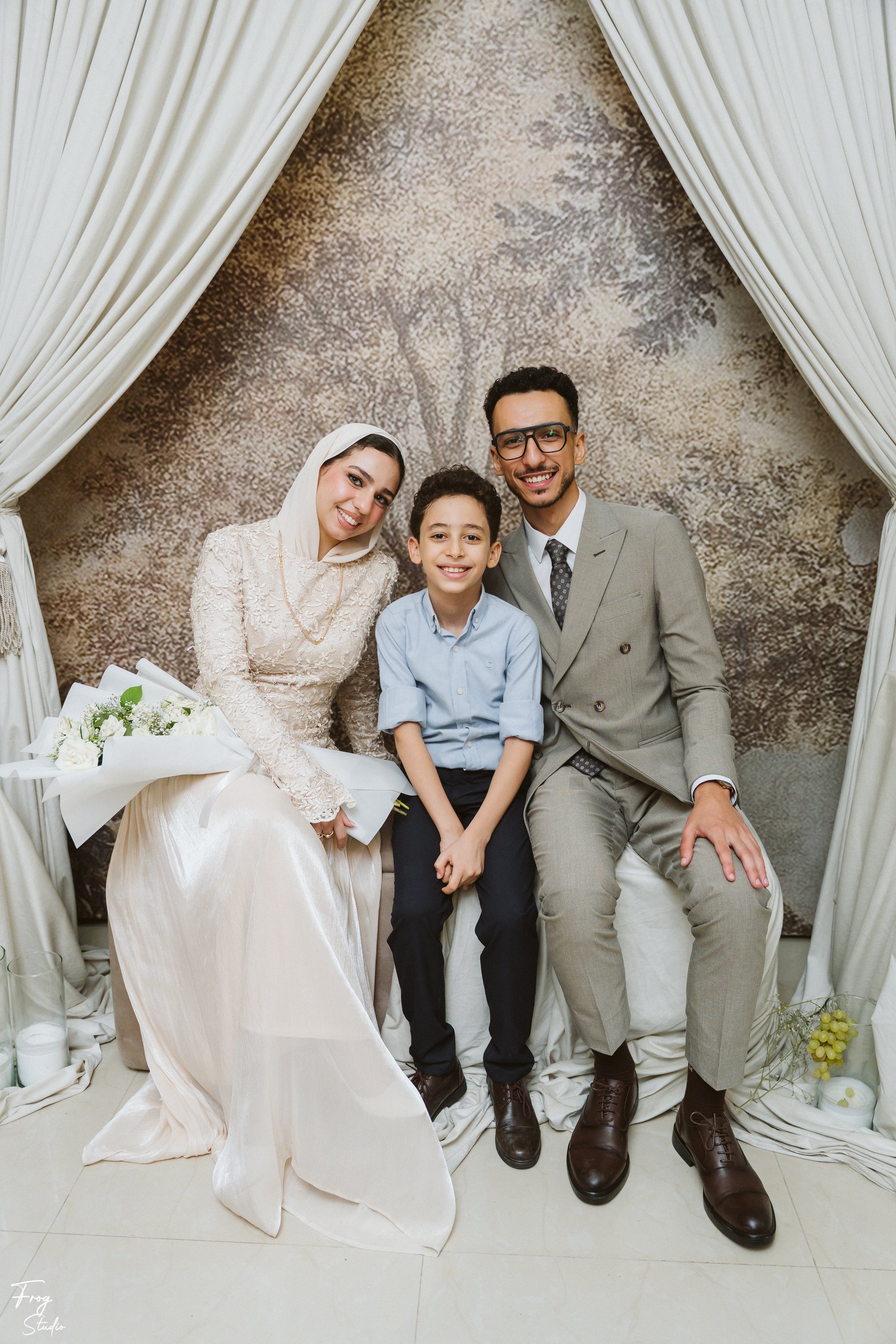 Mohamed and Reem seated with a boy in a light blue shirt, the rose bouquet beside them